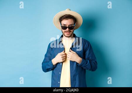 Schöner junger Mann, der in den Urlaub geht, das Hemd anpasst, Sonnenbrille und Strohhut trägt. Konzept des Sommerurlaubs Stockfoto