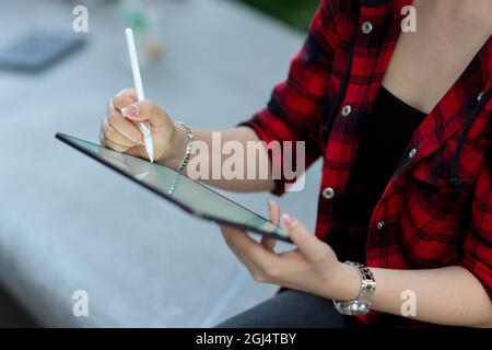 Zugeschnittenes Bild von Hipster Mädchen mit digitalen Tablet mit Stylus-Stift, um digitale Kunstwerke zu schaffen, sitzen in der Stadt Straße Stockfoto