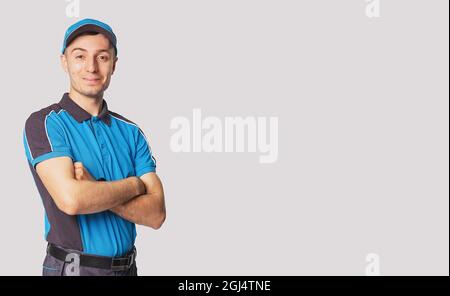 Entbindung Mann mit freudigen Gesichtsausdruck trägt blaue Postmann Uniform stehen mit Kreuzhände, Seite leeren Raum. Stockfoto