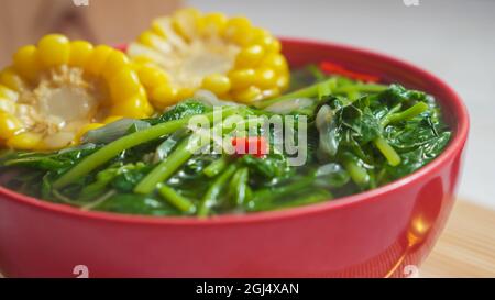 Bekannt als Sayur bening Bayam oder Spinat klare Suppe ist indonesische Lebensmittel aus Spinat, Karotten, Mais und anderen Gemüse. Serviert auf einer roten Schüssel Stockfoto