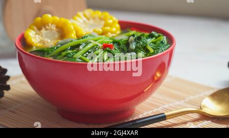 Bekannt als Sayur bening Bayam oder Spinat klare Suppe ist indonesische Lebensmittel aus Spinat, Karotten, Mais und anderen Gemüse. Serviert auf einer roten Schüssel Stockfoto