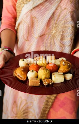 Indische Frau nimmt Diwali Süßigkeiten Gujiya peda barfi Indische süße Dessert mithai Festival Gericht Dussehra Holi ganesh chaturthi RAM navami Durga pooja Stockfoto