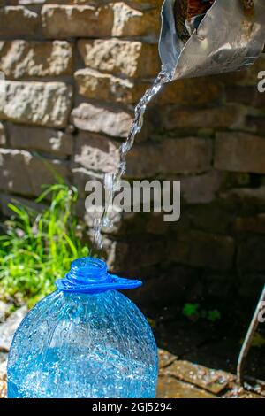 Der Hals einer fünf-Liter-Plastikflasche, in die ein Strom aus reinem, natürlichem, nützlichem, lebensspendenden Wasser aus einer ausgerüsteten, von Menschen hergestellten Quelle gegossen wird Stockfoto