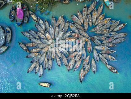 Aus der Vogelperspektive sehen Hunderte von Holzbooten wie Blumen im Buriganga River Port aus. Die mit bunt gemusterten Teppichen geschmückten Boote transportieren Arbeiter aus den Außenbezirken der Stadt zu ihrem Schicksal. Der Buriganga-Fluss wird täglich als Route in die Stadt Dhaka für Millionen von Arbeitern genutzt. Am 9. September 2021 in Dhaka, Bangladesch. (Foto von Mustasinur Rahman Alvi / Eyepix Group) Stockfoto