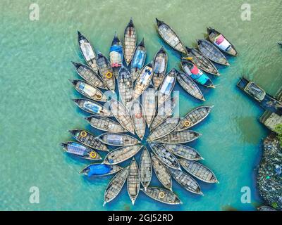 Aus der Vogelperspektive sehen Hunderte von Holzbooten wie Blumen im Buriganga River Port aus. Die mit bunt gemusterten Teppichen geschmückten Boote transportieren Arbeiter aus den Außenbezirken der Stadt zu ihrem Schicksal. Der Buriganga-Fluss wird täglich als Route in die Stadt Dhaka für Millionen von Arbeitern genutzt. Am 9. September 2021 in Dhaka, Bangladesch. (Foto von Mustasinur Rahman Alvi / Eyepix Group) Stockfoto