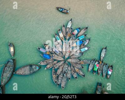 Aus der Vogelperspektive sehen Hunderte von Holzbooten wie Blumen im Buriganga River Port aus. Die mit bunt gemusterten Teppichen geschmückten Boote transportieren Arbeiter aus den Außenbezirken der Stadt zu ihrem Schicksal. Der Buriganga-Fluss wird täglich als Route in die Stadt Dhaka für Millionen von Arbeitern genutzt. Am 9. September 2021 in Dhaka, Bangladesch. (Foto von Mustasinur Rahman Alvi / Eyepix Group) Stockfoto