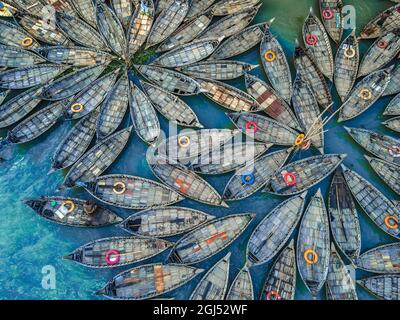 Aus der Vogelperspektive sehen Hunderte von Holzbooten wie Blumen im Buriganga River Port aus. Die mit bunt gemusterten Teppichen geschmückten Boote transportieren Arbeiter aus den Außenbezirken der Stadt zu ihrem Schicksal. Der Buriganga-Fluss wird täglich als Route in die Stadt Dhaka für Millionen von Arbeitern genutzt. Am 9. September 2021 in Dhaka, Bangladesch. (Foto von Mustasinur Rahman Alvi / Eyepix Group) Stockfoto