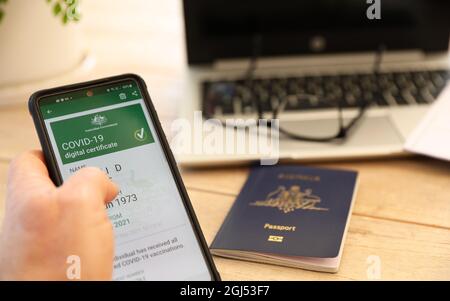 Offizieller digitaler Nachweis des Impfzertifikats covid-19 auf einem Mobiltelefon der australischen Regierung. Reisepass im Hintergrund und Laptop verschwommen Stockfoto