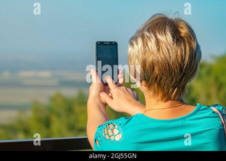 Der Blick eines Mädchens von hinten, das auf einem Smartphone Bilder von der Landschaft macht und mit dem Finger den Bildschirm berührt Stockfoto
