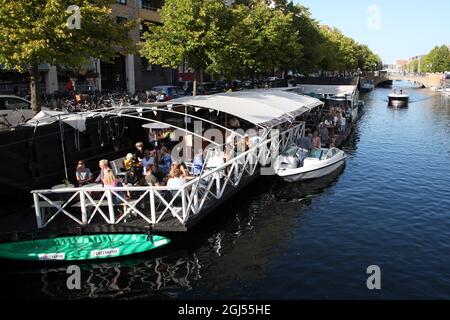 Kopenhagen, Dänemark. September 2021. Im Kopenhagener Stadtteil Christianshavn sitzen die Leute in einer Bar an einem Kanal, während ein Boot vorbeifährt. Dänemark hebt die verbleibenden Corona-Maßnahmen im Land am 10. September auf. Schon jetzt fühlt sich das Leben in der Hauptstadt Kopenhagen fast restriktionsfrei an. (To dpa 'Denmark says Auf Wiedersehen to Last Corona restrictions') Quelle: Steffen TRUMPF/dpa/Alamy Live News Stockfoto