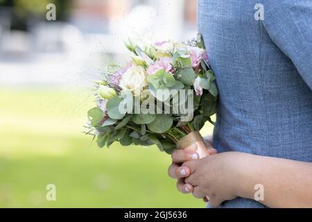 Nahaufnahme der Hand einer Braut mit einem Bouquet aus weißen und rosa Rosen, die die blaue Weste des Bräutigams auf einem Wiesenhintergrund umarmen. Hochwertige Fotos Stockfoto