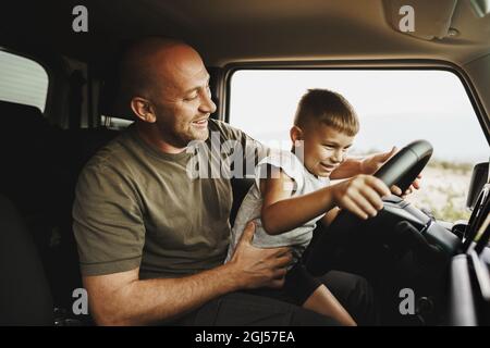 Vater lehrt den kleinen Sohn auf einer Autoreise zu fahren Stockfoto