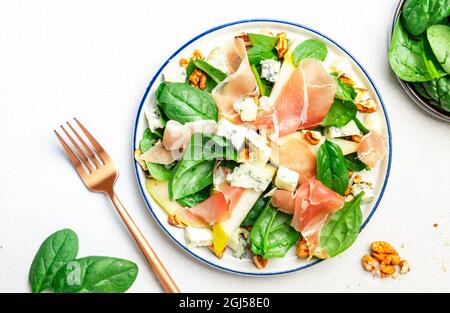 Birnensalat mit Prosciutto, Blauschimmelkäse, Spinat, Walnüssen auf weißem Hintergrund, Draufsicht, Kopierraum Stockfoto