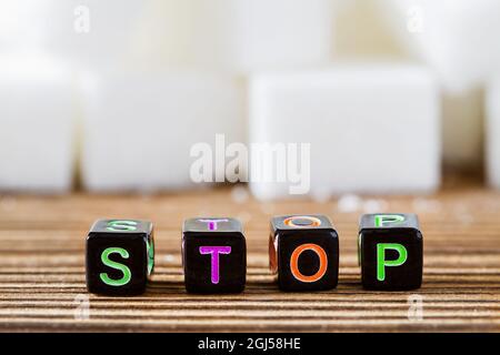 Das Wort STOP auf dem Hintergrund von weißen Zuckerwürfeln. Stoppen Sie das Konzept des weißen Zuckers. Nahaufnahme, selektiver Fokus. Stockfoto