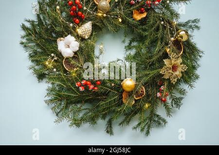 Weihnachtskomposition. Handgefertigter weihnachtskranz aus Tannenzweigen. Draufsicht, flach liegend. Blauer Hintergrund, Beeren, Orangen- und Apfelscheiben als Dekoration Stockfoto