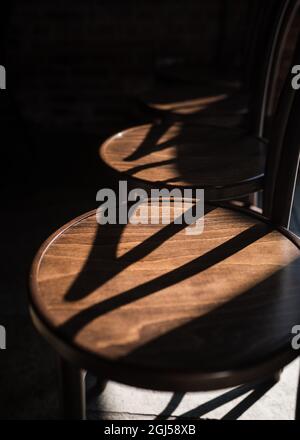 Die Sonne scheint über eine Reihe von Vintage-Holzsitzen und wirft Schatten in einem wunderschönen rustikalen, alten Hochzeitslokal. Keine Menschen, leer und ruhig. Stockfoto