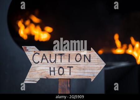 Vorsicht Warnung heißer Holzpfeilschild mit orangefarbenem Feuer und Flammen im Hintergrund. Gefahr von gefährlichen Verbrennungen durch feurige Flammen im Hintergrund. Stockfoto