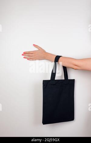 Eco-Bag mit weiblicher Hand. Modell eines kleinen, wiederverwendbaren schwarzen Ökobeutels aus recycelten Materialien auf weißem, isoliertem Hintergrund, Konzept der Zero Waste Stockfoto