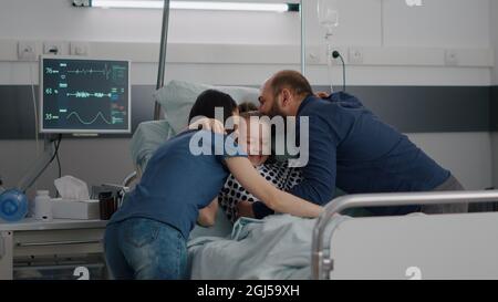 Glückliche Eltern besuchen kranke Tochter umarmen Kind während der Untersuchung auf der Krankenstation. Hospitalisiertes Kind mit Sauerstoff-Nasenschlauch, der nach einer Genesungsoperation im Bett ruht Stockfoto