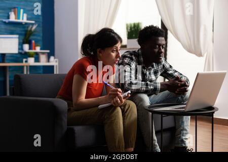 Interracial paar Berechnung Steuergeld mit Laptop für Wirtschaft und Budget. Junge, multiethnische Partner mit Notebook, die Steuern und Finanzbuchhaltung für Zahlungen zu Hause erledigen. Stockfoto
