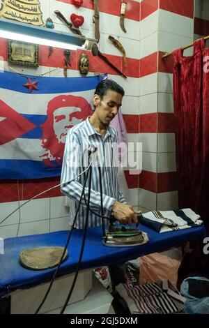Spaziergang durch den Souk in der Nacht. Mann arbeitet mit Che-Flagge an Bügelkleidung. Assuan, Ägypten. Stockfoto