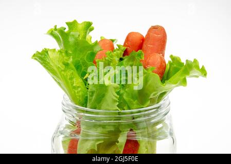 Salatblätter und Karotten in einer transparenten Glasflasche auf hellem Hintergrund Stockfoto