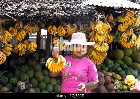 Afrika, Madagaskar, in der Nähe von Andesit, Alaotra-Mangoro-Region. Eine Frau mit Paste auf ihrem Gesicht, die als Sonnenschutzmittel fungiert, kauft Bananen. Stockfoto