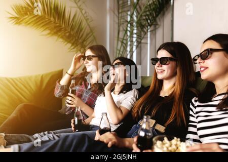 Eine Gruppe von Freunden in 3D-Brillen schaut sich einen Film an, lächelt, lacht. Essen und Trinken, während Sie sich einen Film im Kino ansehen. Mädchen essen Popc Stockfoto