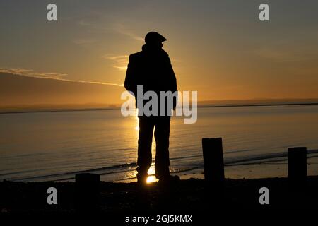 Ein Mann beobachtet den Sonnenuntergang über dem Solent auf Hayling Island, Hampshire, Großbritannien Stockfoto