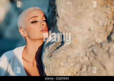 Porträt einer jungen, tausendjährigen europäischen Kurzhaarigen. Schöne glücklich blonde Mädchen auf Stein Rock im Freien. Sommermode Damenbekleidung. Stockfoto