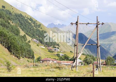 Großer Energiemast aus Holz mit Drähten und Berglandschaft unter Sonnenlicht Stockfoto