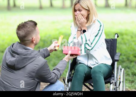 Der junge Mann schenkt der glücklichen Frau im Rollstuhl ein Geschenk Stockfoto