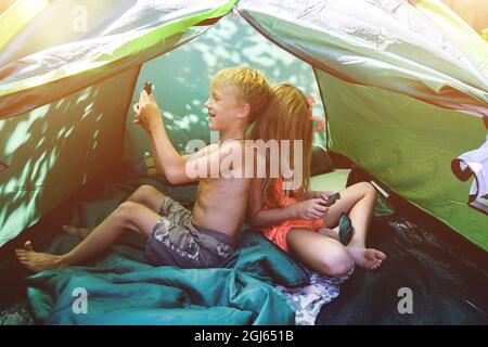 Junge und Mädchen in einem Zelt mit Mobiltelefonen Stockfoto