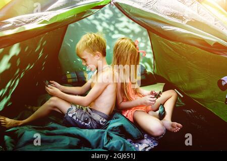 Junge und Mädchen in einem Zelt mit Mobiltelefonen Stockfoto