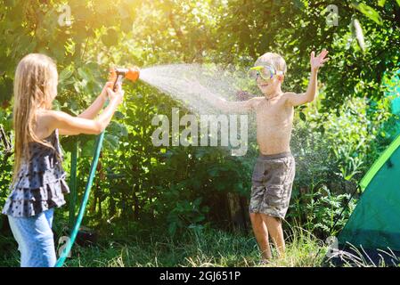 Junge mit einem Mädchen, das im heißen Sommer spielt, sich gegenseitig mit Wasser aus einem Gartenschlauch sprüht.Toning.Focus on boy Stockfoto