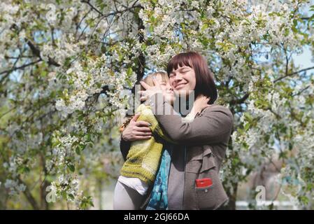 Die Tochter umarmt ihre Mutter liebevoll. Hintergrund - ein blühender Frühlingsbaum Stockfoto
