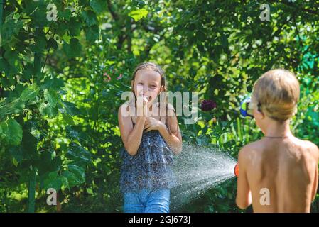 Junge mit einem Mädchen, das im heißen Sommer spielt und sich gegenseitig mit Wasser aus einem Gartenschlauch sprüht.Toning.Focus on girl Stockfoto