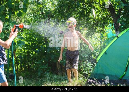 Junge mit einem Mädchen, das im heißen Sommer spielt, sich gegenseitig mit Wasser aus einem Gartenschlauch sprüht.Toning.Focus on boy Stockfoto