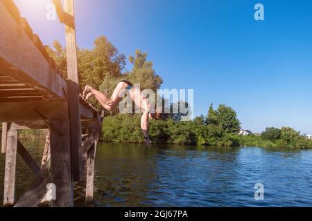 Der Junge springt von einer Holzbrücke ins Wasser Stockfoto