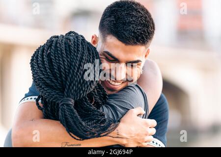 Nahaufnahme eines kaukasischen Mannes, der eine Afro-Frau umarmt und im Freien lächelt Stockfoto