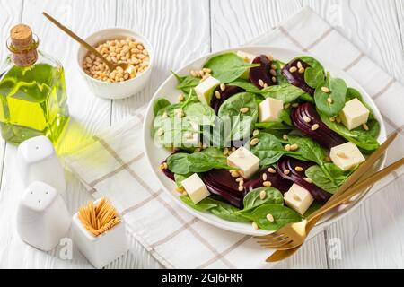 Gerösteter Rübensalat mit gewürfeltem Feta-Käse, Pinienkernen und Spinat auf einem weißen Teller mit goldenem Besteck auf einem Holztisch, kanadische Küche Stockfoto