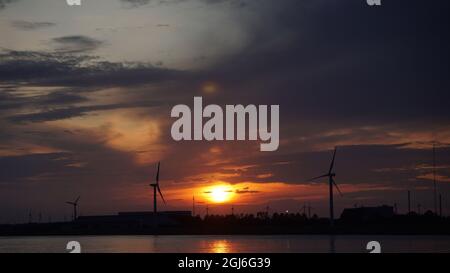 Silhouetten von Windkraftanlagen und Kränen im Hafen bei Sonnenuntergang, Hamburg, Deutschland Stockfoto