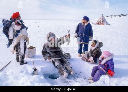 Baker Lake, Nunavut, Kanada. Besucherin in traditioneller Karibu-Kleidung versucht sich im Lager beim Angeln. Inuit Ältere und Inuit Kinder Stockfoto