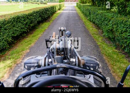 Blick von der Kabine aus auf einen Allradantrieb-Radlader mit Gabelstaplern, der in einem ländlichen lan gefahren wird Stockfoto