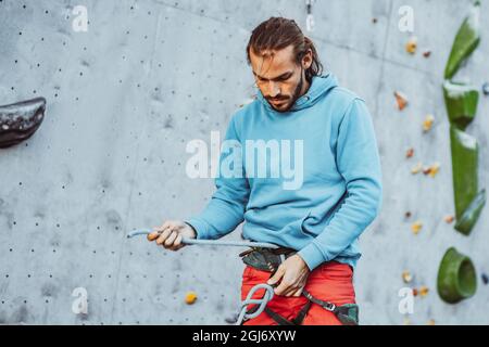 Junger Profi-Kletterer überprüft Sportausrüstung, bevor er im Trainingszentrum an sonnigen Tagen im Freien klettert. Konzept eines gesunden Lebensstils Stockfoto