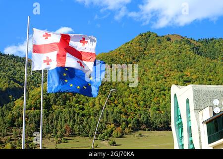 Georgische Flagge mit EU-Flagge, die gegen die frühen Herbstberge der Stadt Mestia, Region Svaneti, Georgien winkt Stockfoto