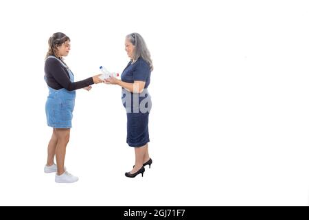 Teenagermädchen, die ihre Plastikflasche ihrer reifen Mutter gibt, damit sie sie in den Papierkorb legen kann, Umweltbewusstsein, leichtes Make-up, lockerer Stil, Stockfoto