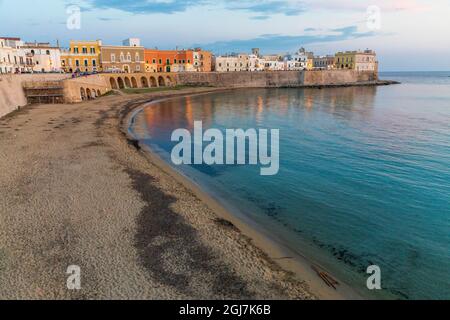 Italien, Apulien, Provinz Lecce, Gallipoli. Strand und Altstadt über das Ionische Meer bei Sonnenuntergang. Stockfoto