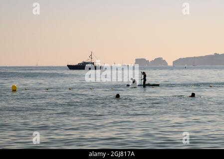 Paddlebarder, Schwimmer und Boote mit Old Harry Rocks an einem heißen Spätsommertag vor Knoll Beach, Shell Bay, Studland, Purbeck, Dorset, VEREINIGTES KÖNIGREICH Stockfoto