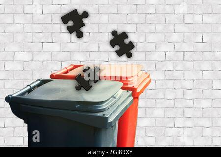 Mülltonne mit Puzzles-Stücken auf weißem Backstein-Hintergrund. Separates Konzept zur Sammlung von Garbage. Puzzle hat sich entwickelt Stockfoto